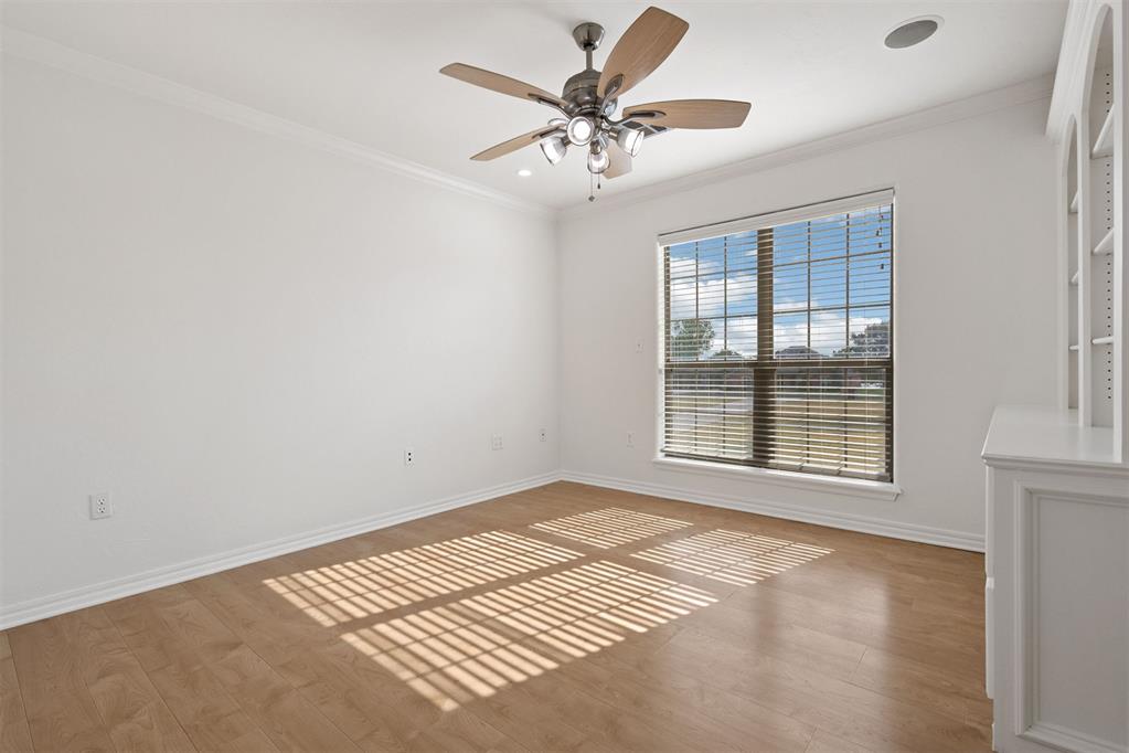 Empty room with wood floors, a ceiling fan, and sunlight through a large window with blinds.
