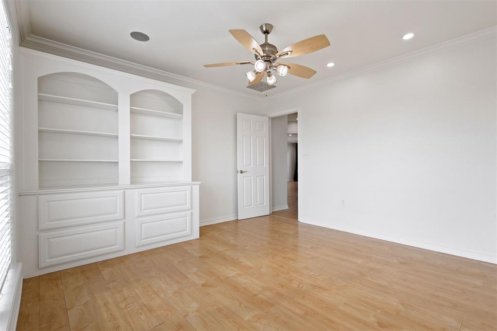 Empty room with built-in shelves and drawers, light wood flooring, and a ceiling fan.