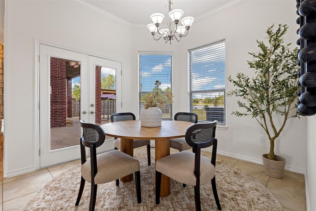 Dining room with a round wooden table, French doors, bright windows, and a potted tree.