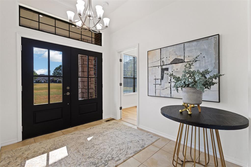 Staged entryway with black double doors, a transom window, chandelier, and round console table.
