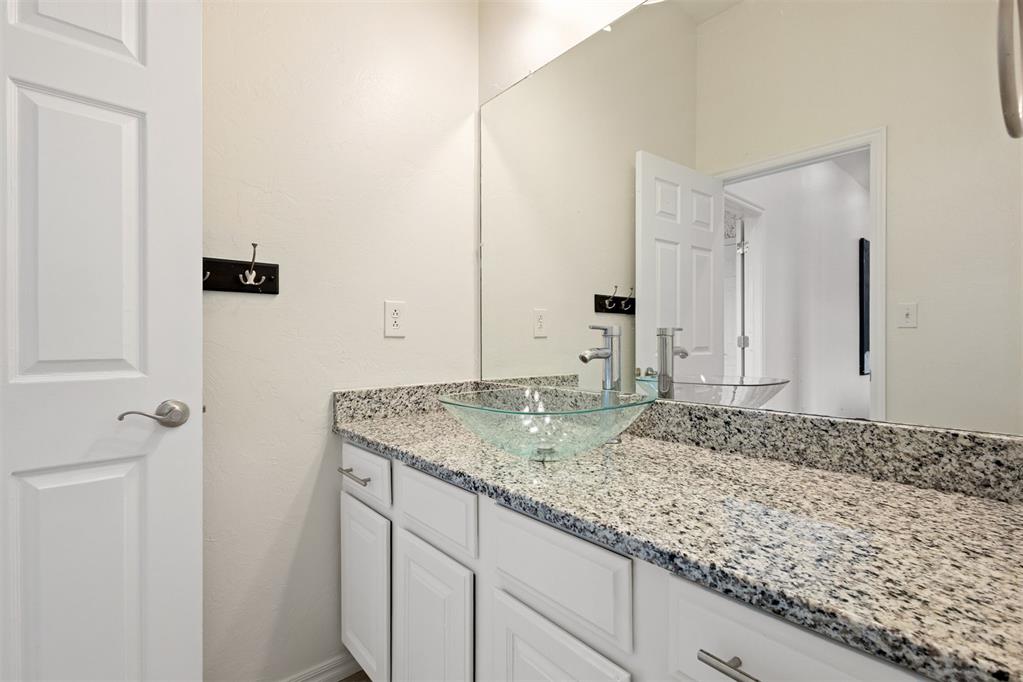 Bathroom vanity with a clear glass vessel sink and speckled granite countertop.
