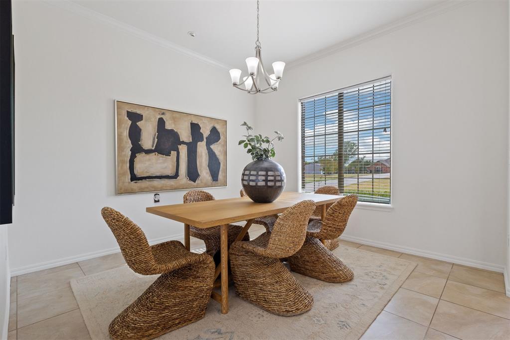 Dining room with a wood table, woven wicker chairs, and a chandelier beside a large window.