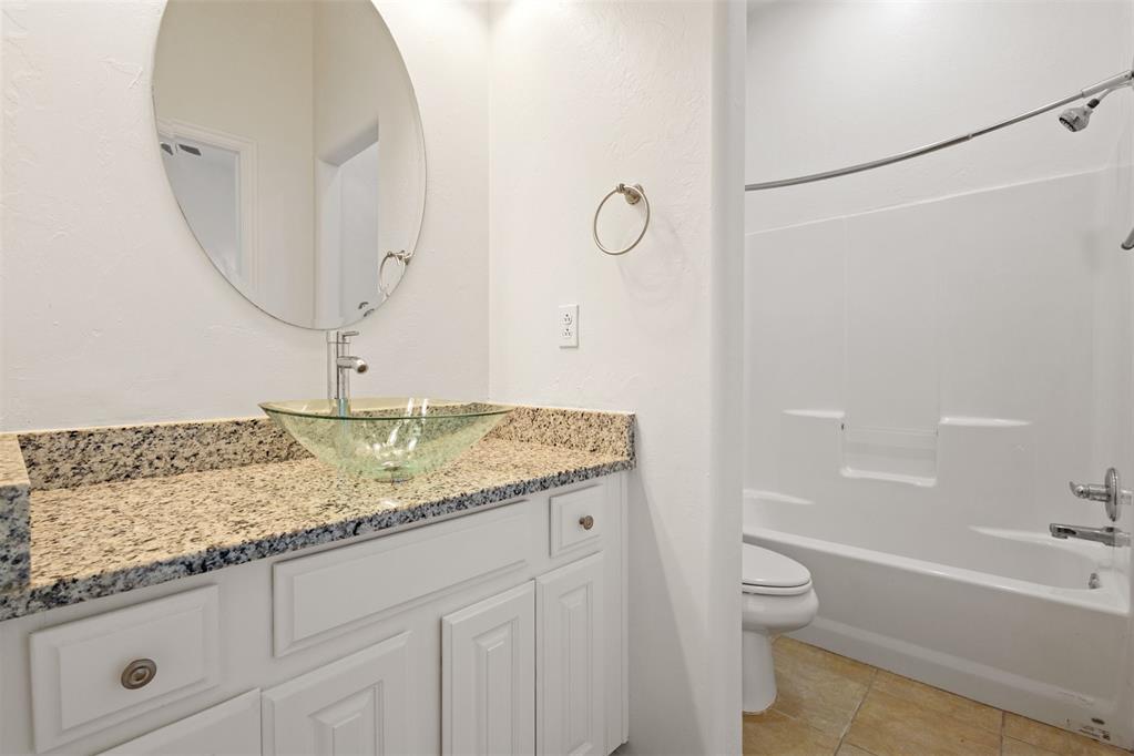 Bathroom with a granite-topped vanity, green glass vessel sink, oval mirror, toilet, and bathtub.