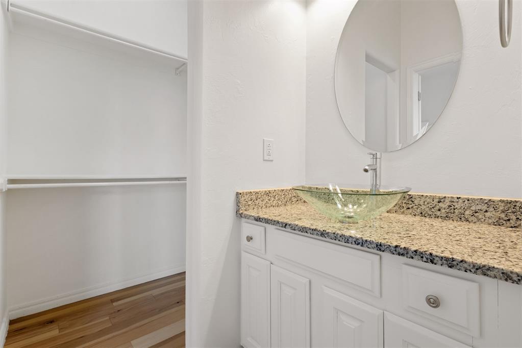 Bathroom vanity with a glass vessel sink and round mirror beside an open closet.