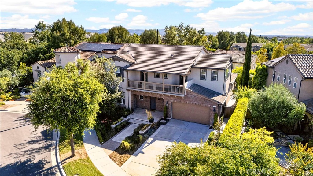 Aerial view of a two-story home with solar panels, a front balcony, and landscaped grounds.