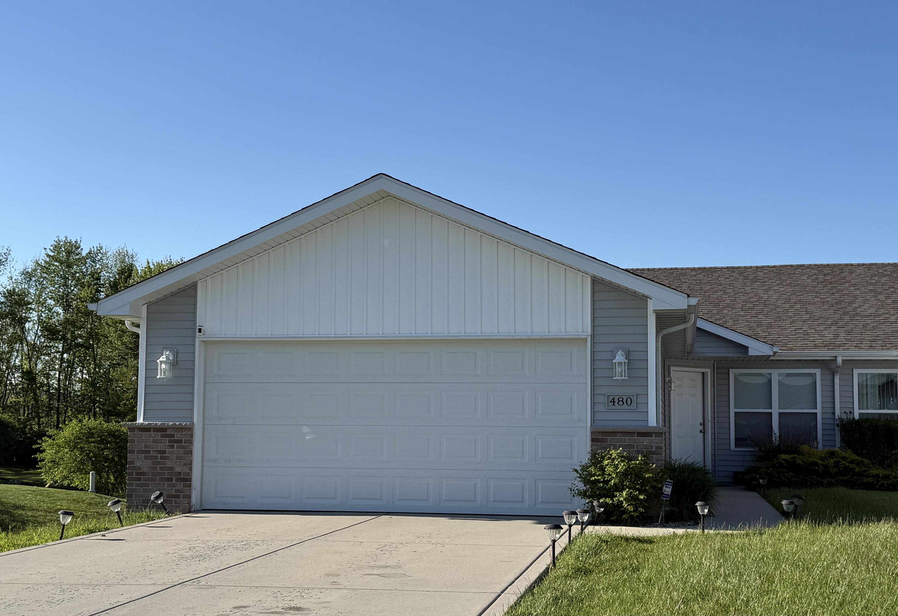Gray single-story home with white trim, large double garage door, and concrete driveway.