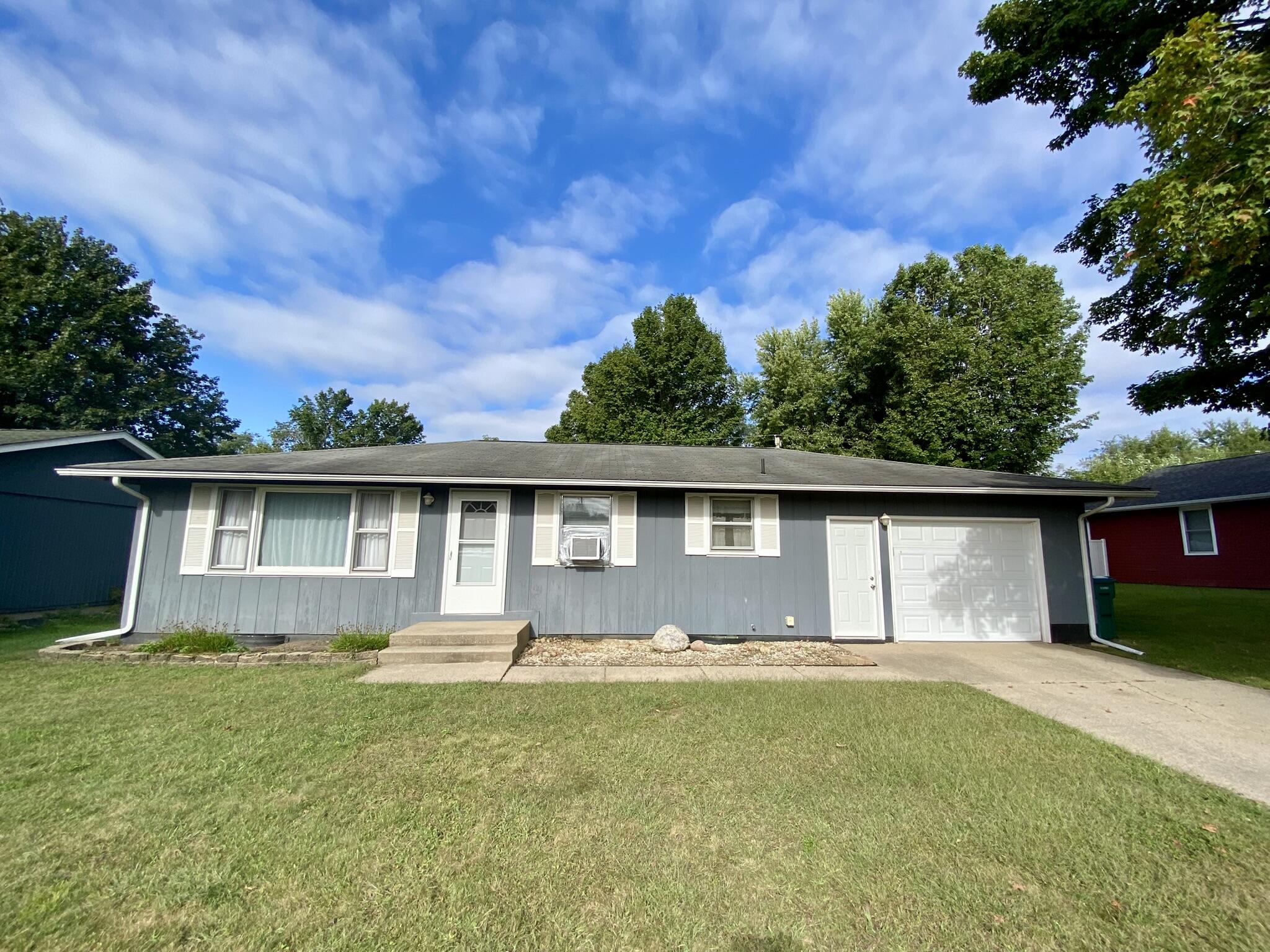 Single-story gray home with white trim, an attached garage, and a broad front lawn.