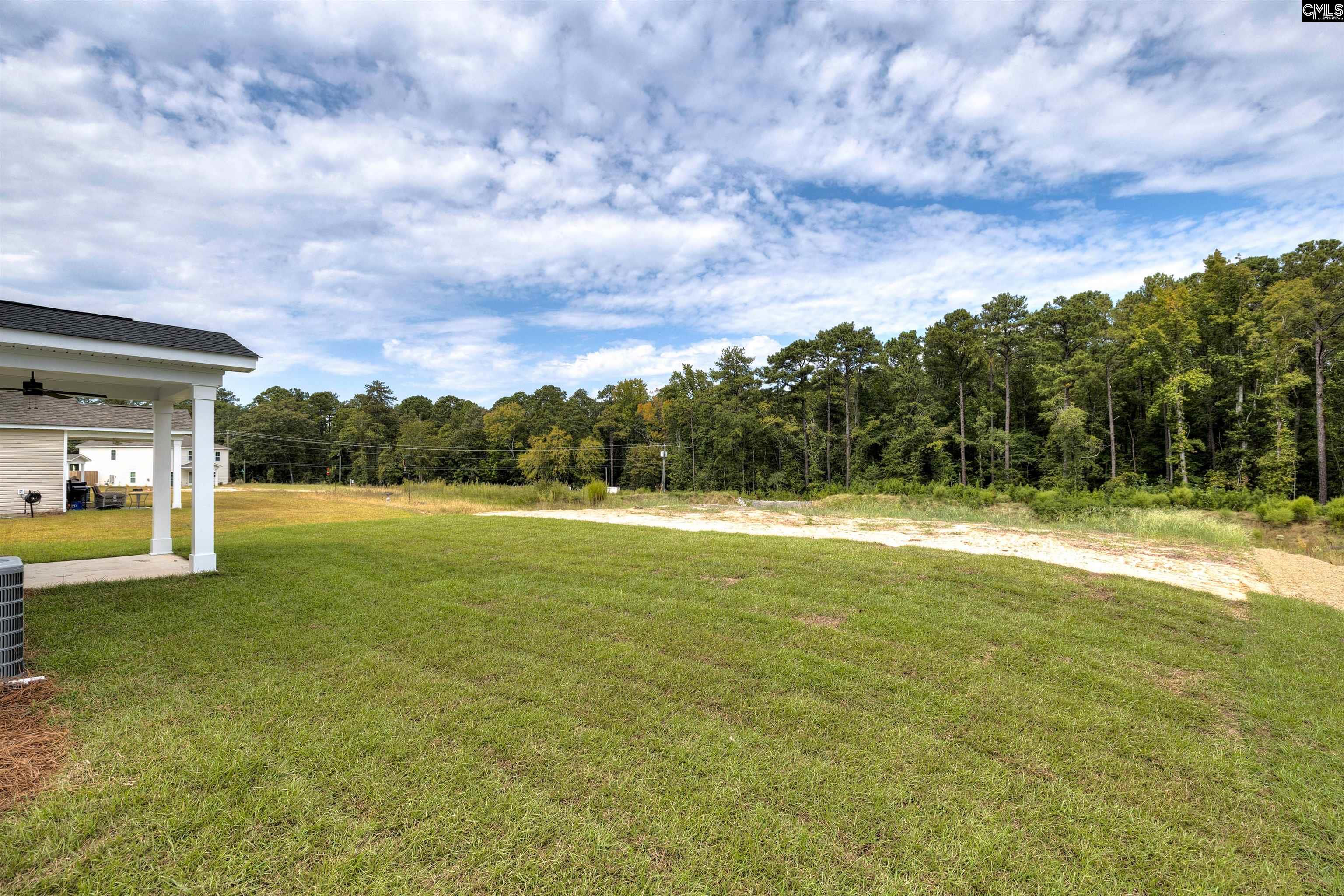 Grassy backyard with a covered patio and wooded tree line.