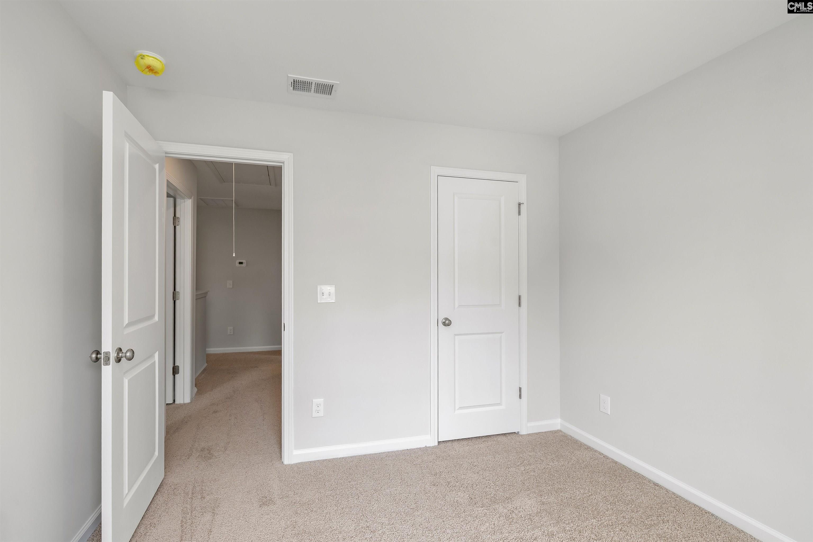 Empty carpeted bedroom with light gray walls and an open doorway beside a closed closet door.