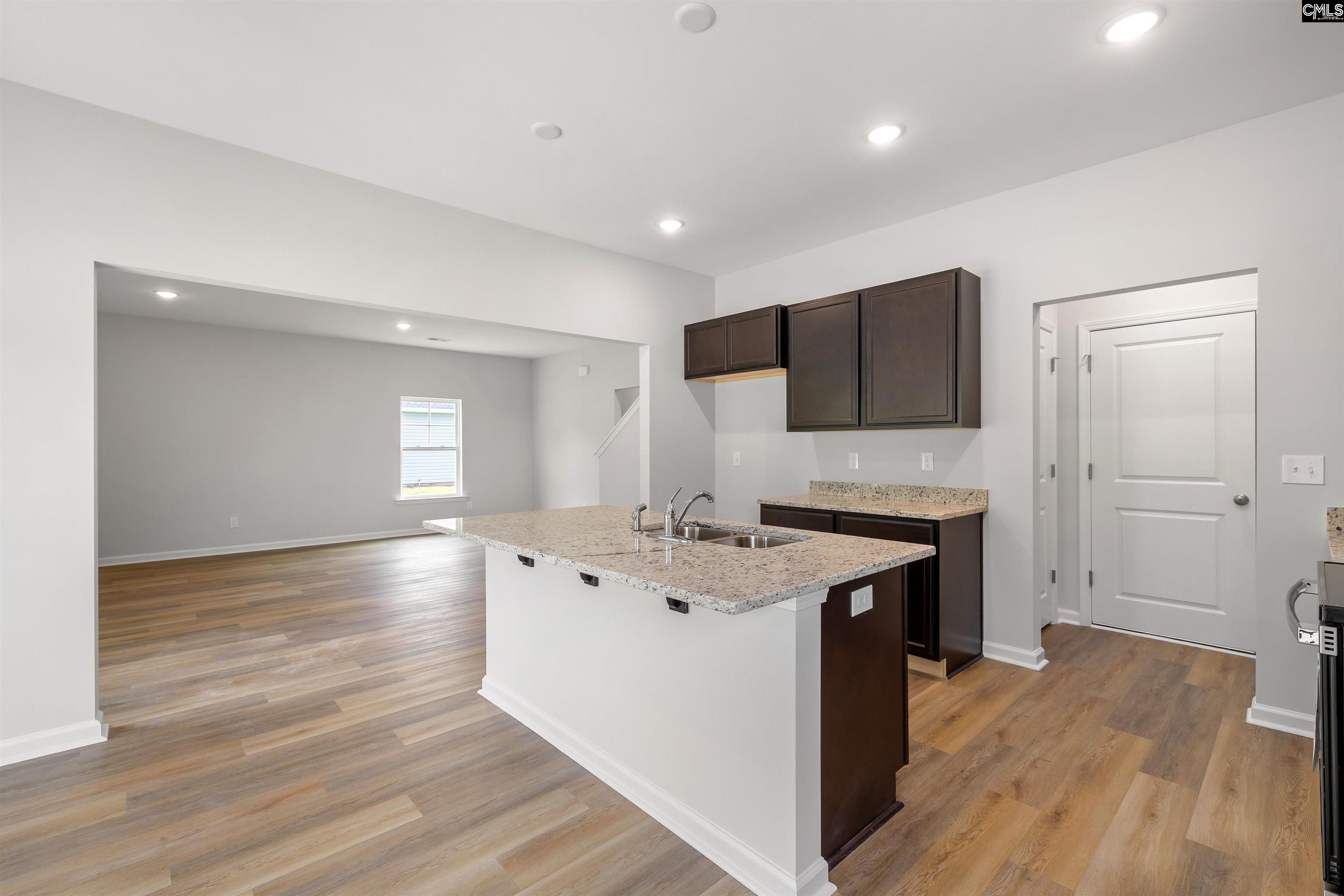 Open kitchen with granite peninsula and dark cabinets, adjoining a bright living area with wood-look floors.