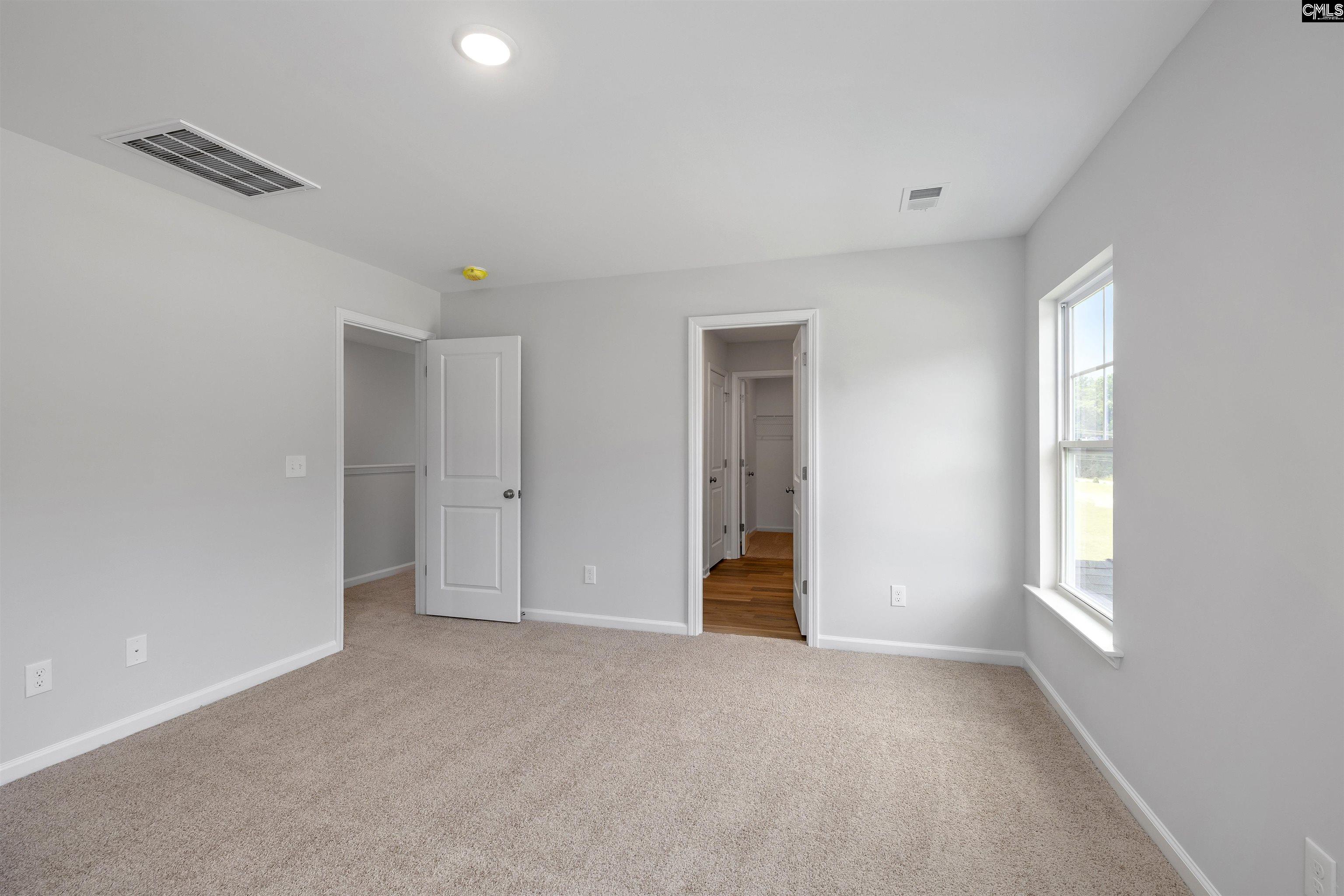 Empty carpeted bedroom with gray walls, a large window, and open doorways.