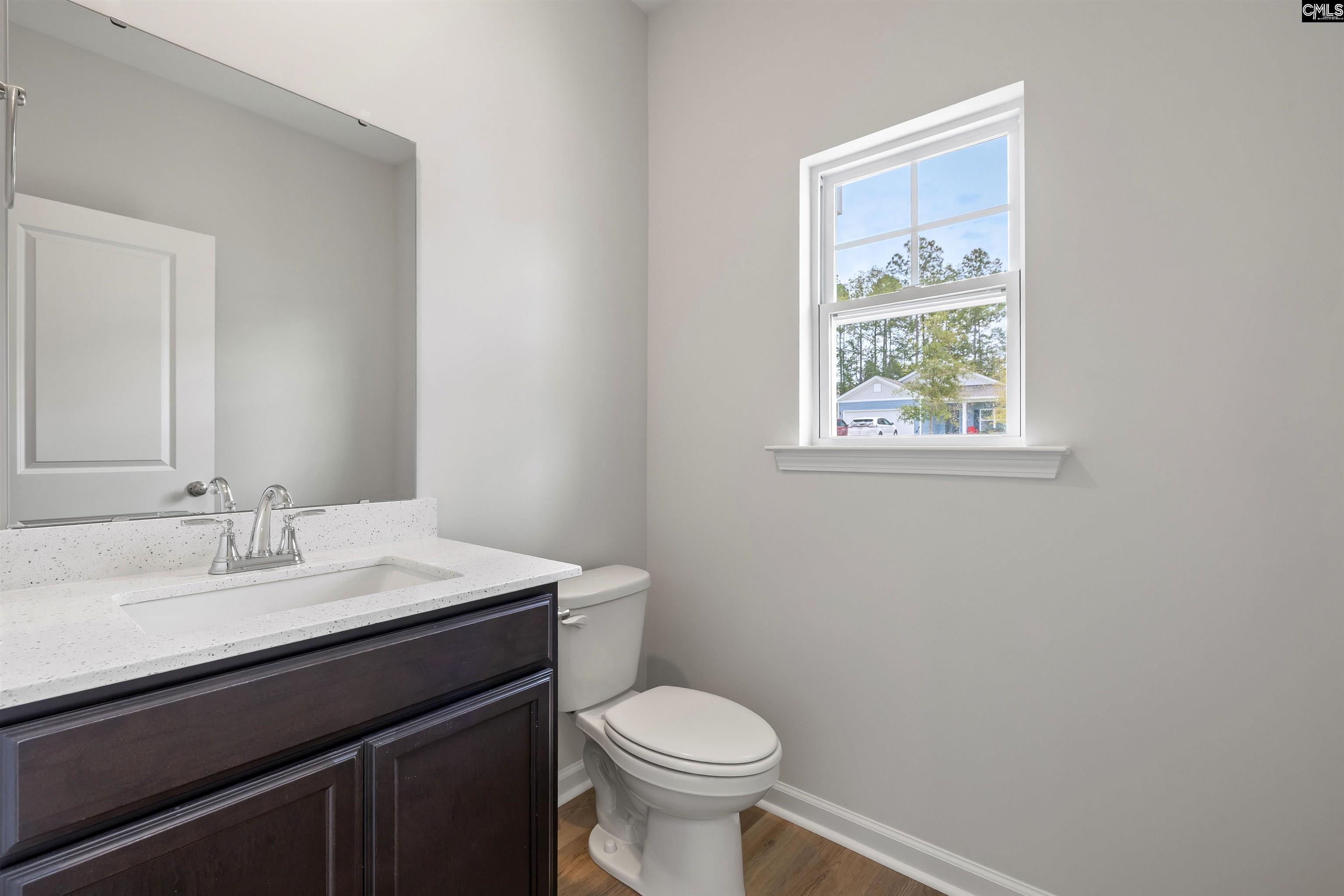 Bathroom with a dark wood vanity, white countertop, toilet, and a window overlooking trees.