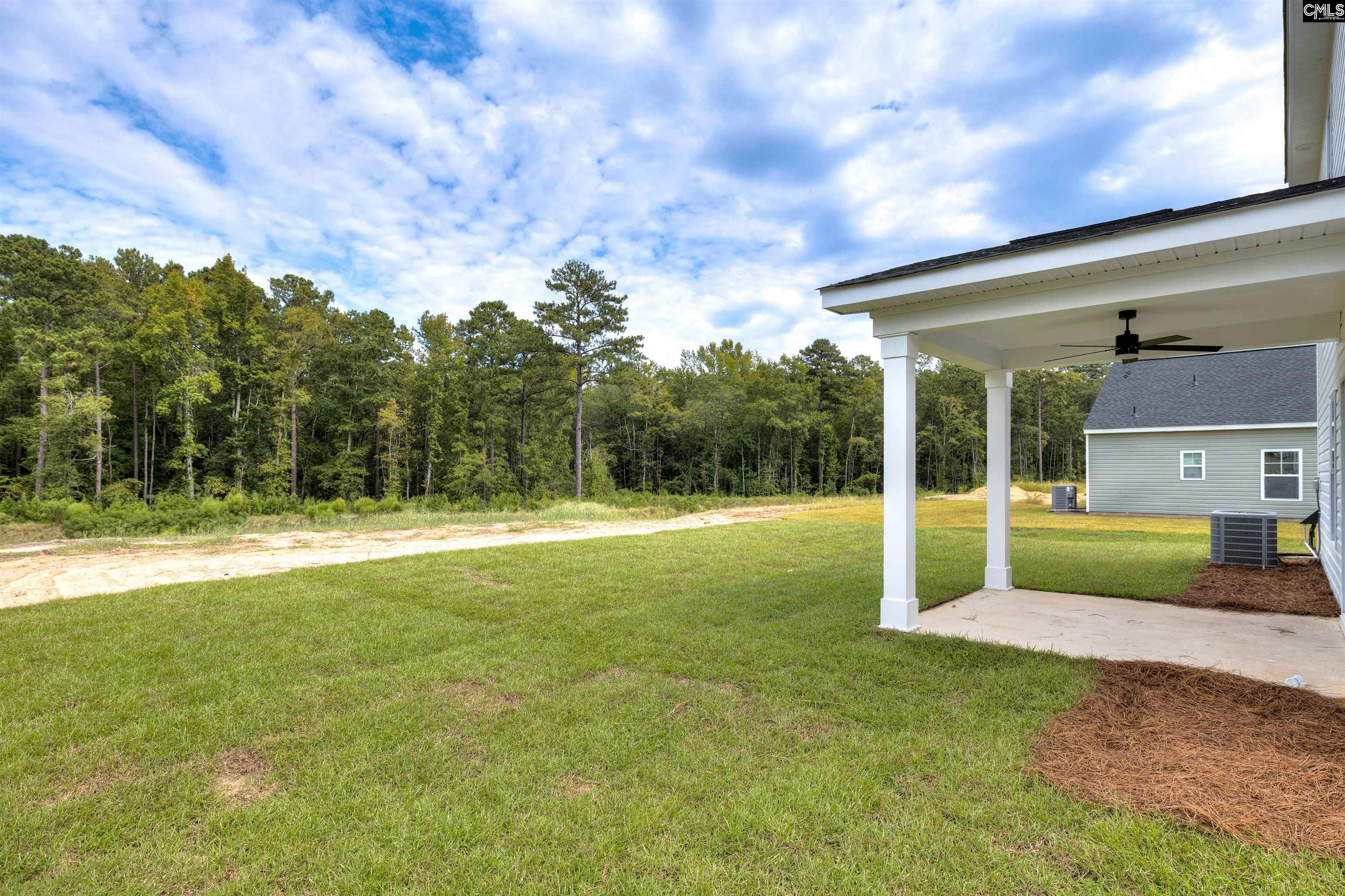 Backyard with a covered patio and lawn bordered by trees.