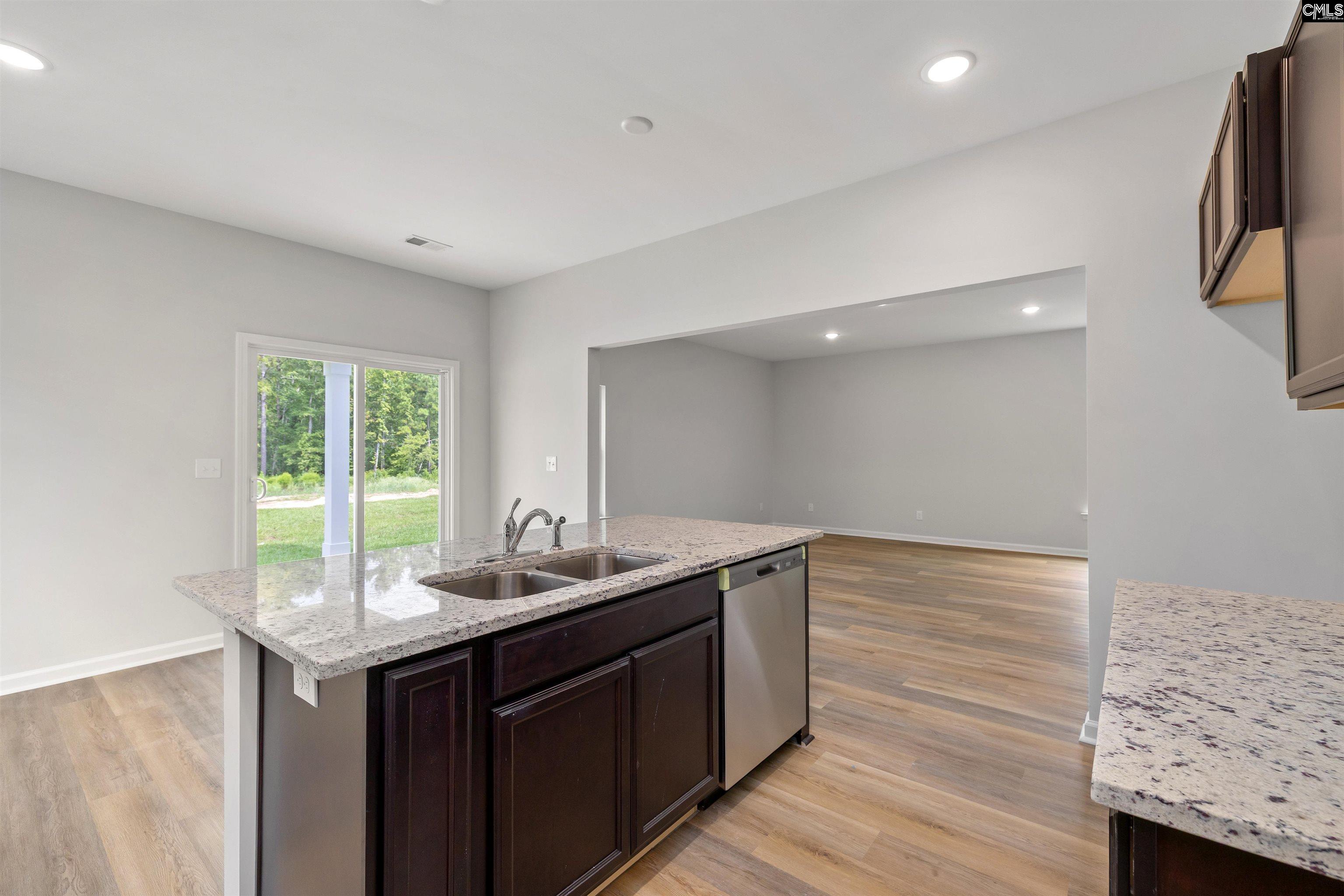 Vacant kitchen with a granite island, double sink, dishwasher, and sliding glass door to the yard.