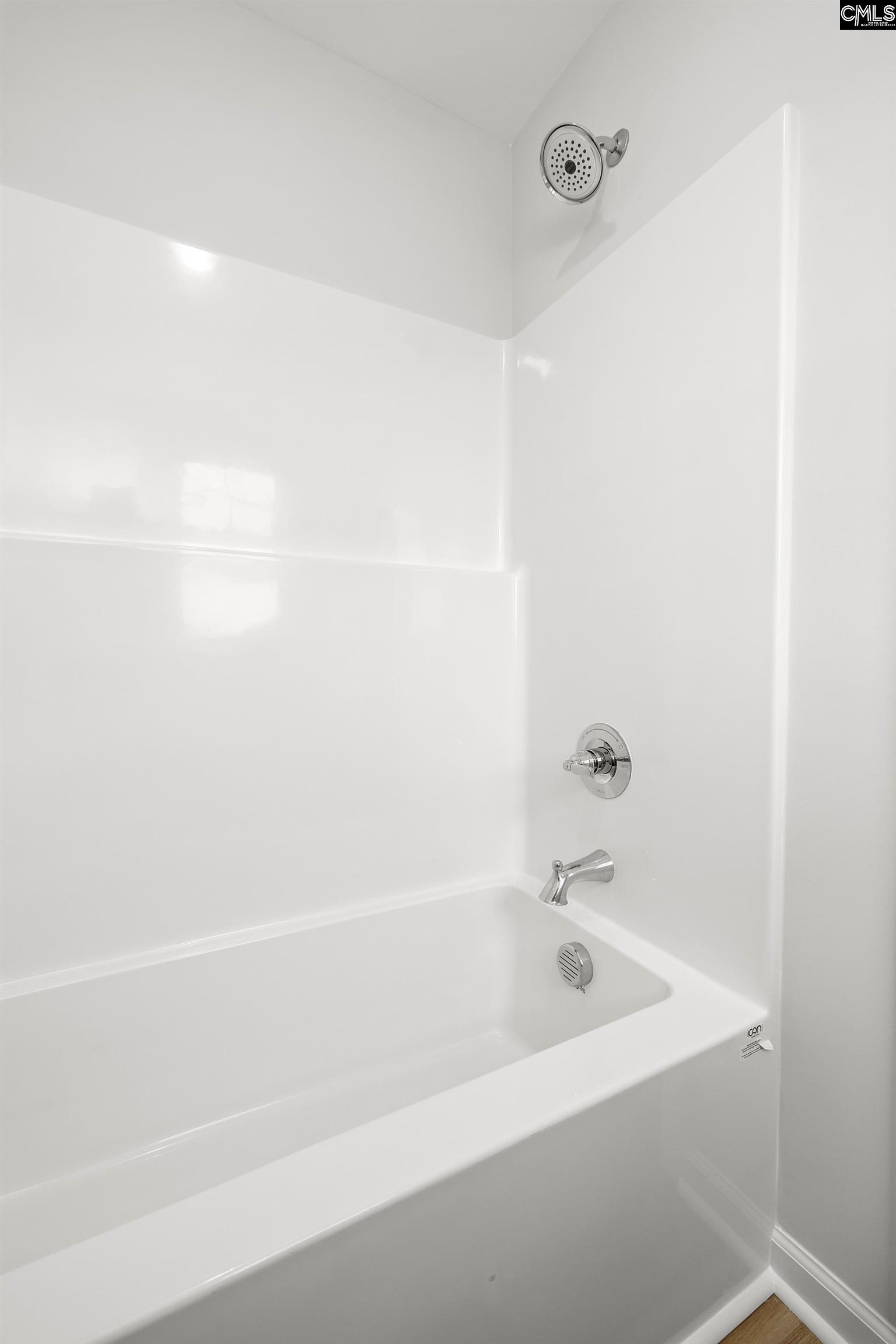 White bathtub and shower with a glossy surround and chrome fixtures.