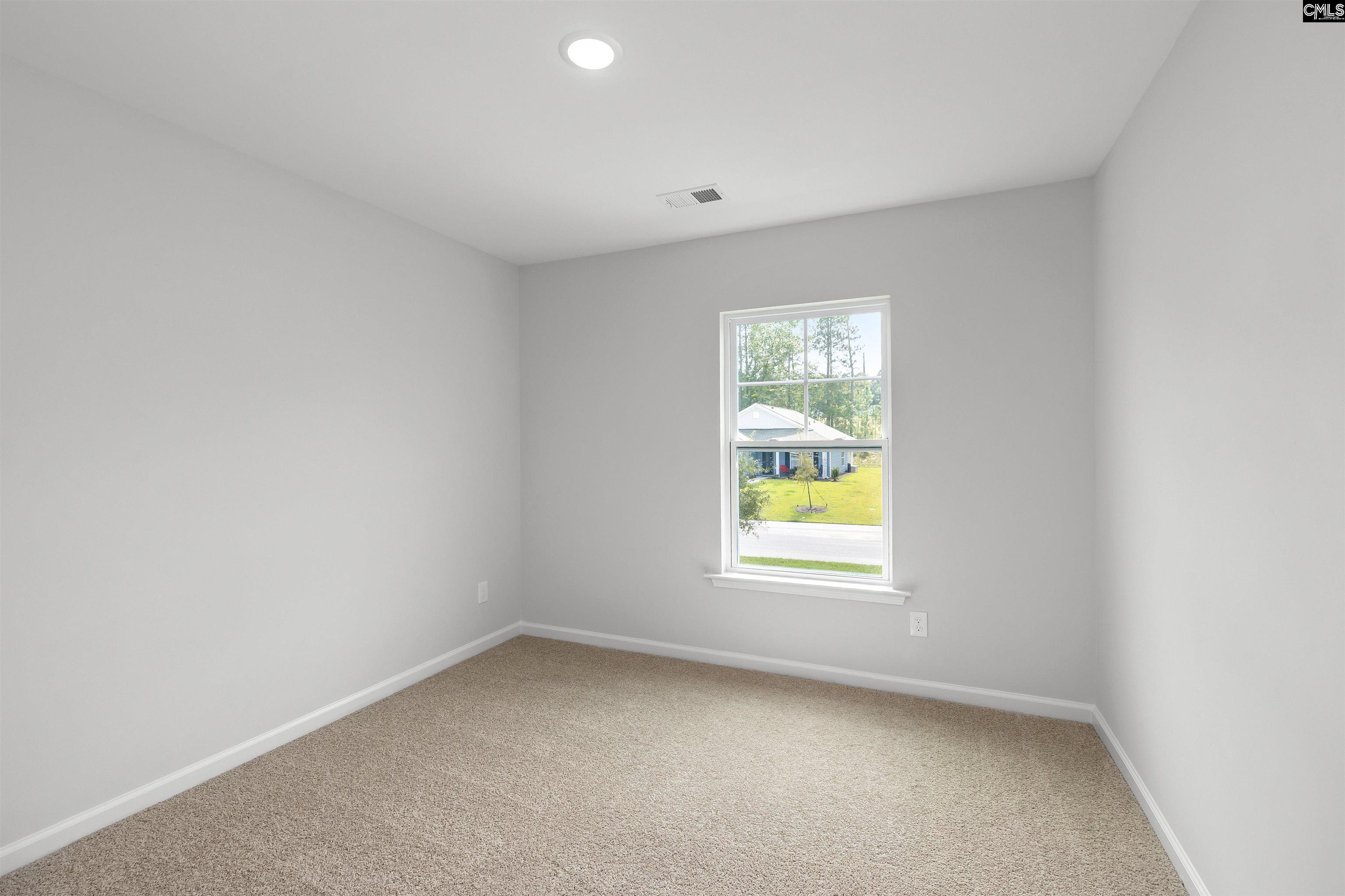 Vacant bedroom with beige carpet and a window overlooking a neighboring home.