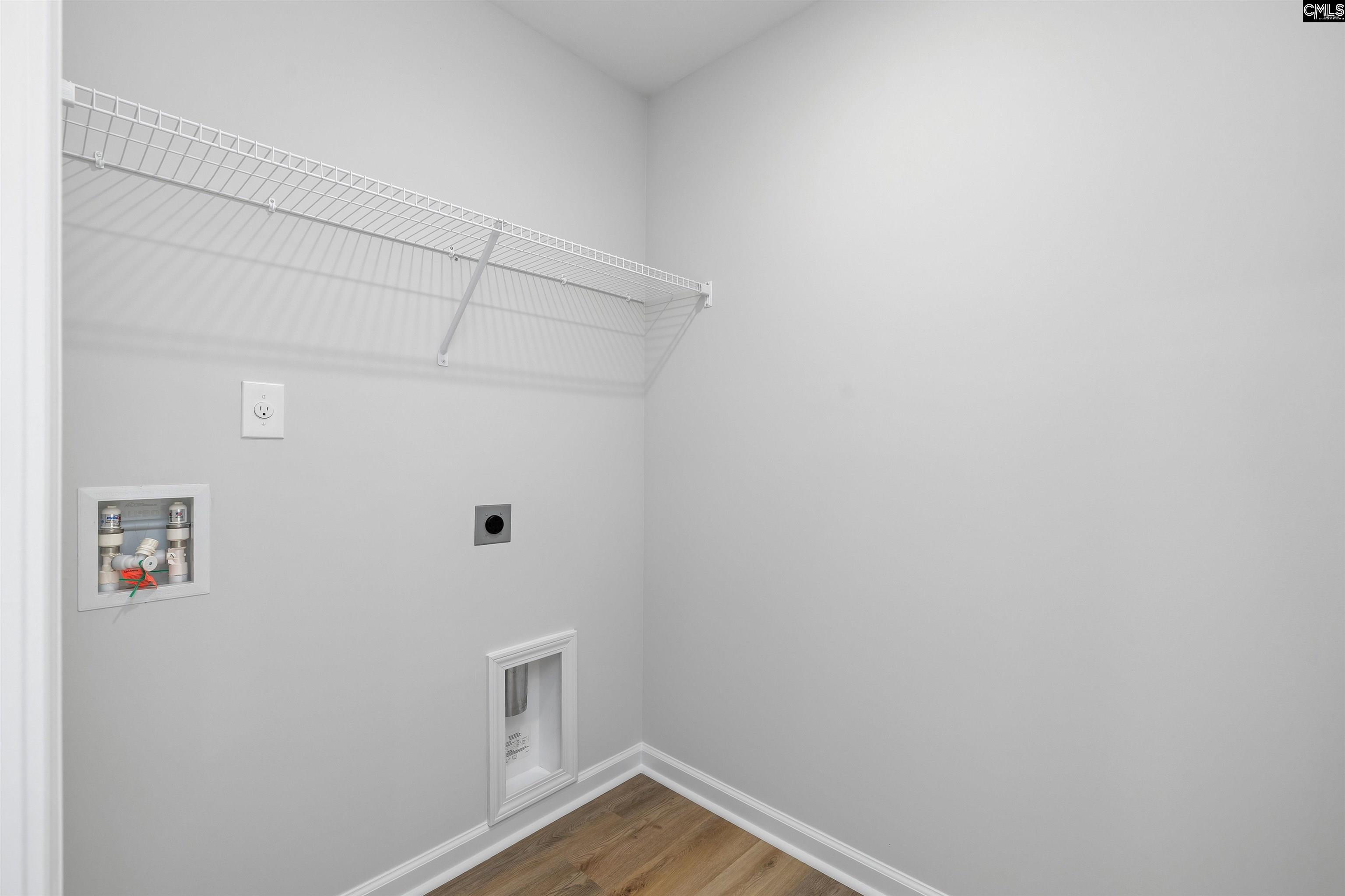 Empty laundry room with a white wire shelf, appliance hookups, and wood-look flooring.