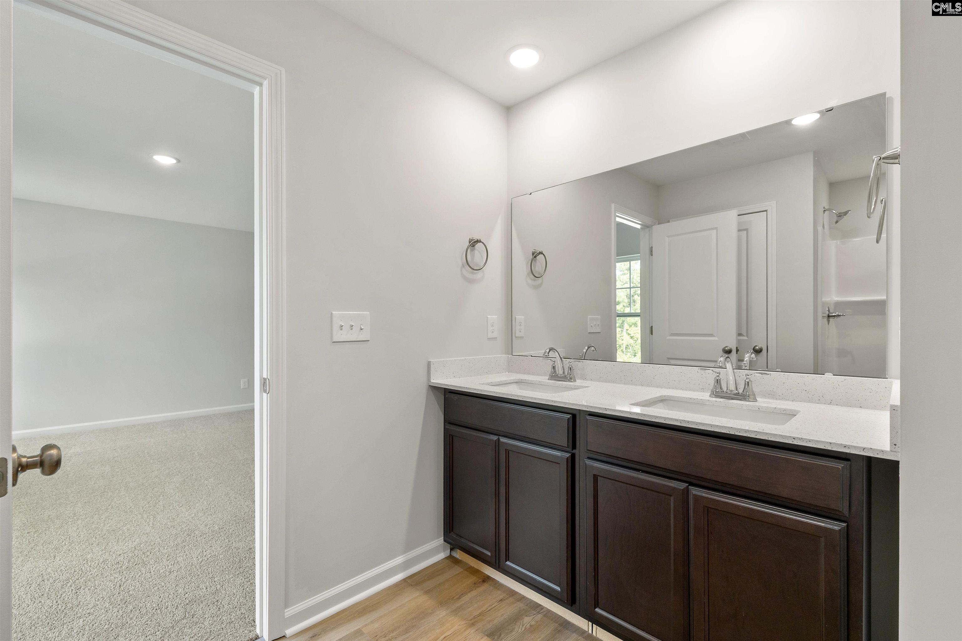 Bathroom with a dark double vanity, two sinks, and a wide mirror beside an open doorway.