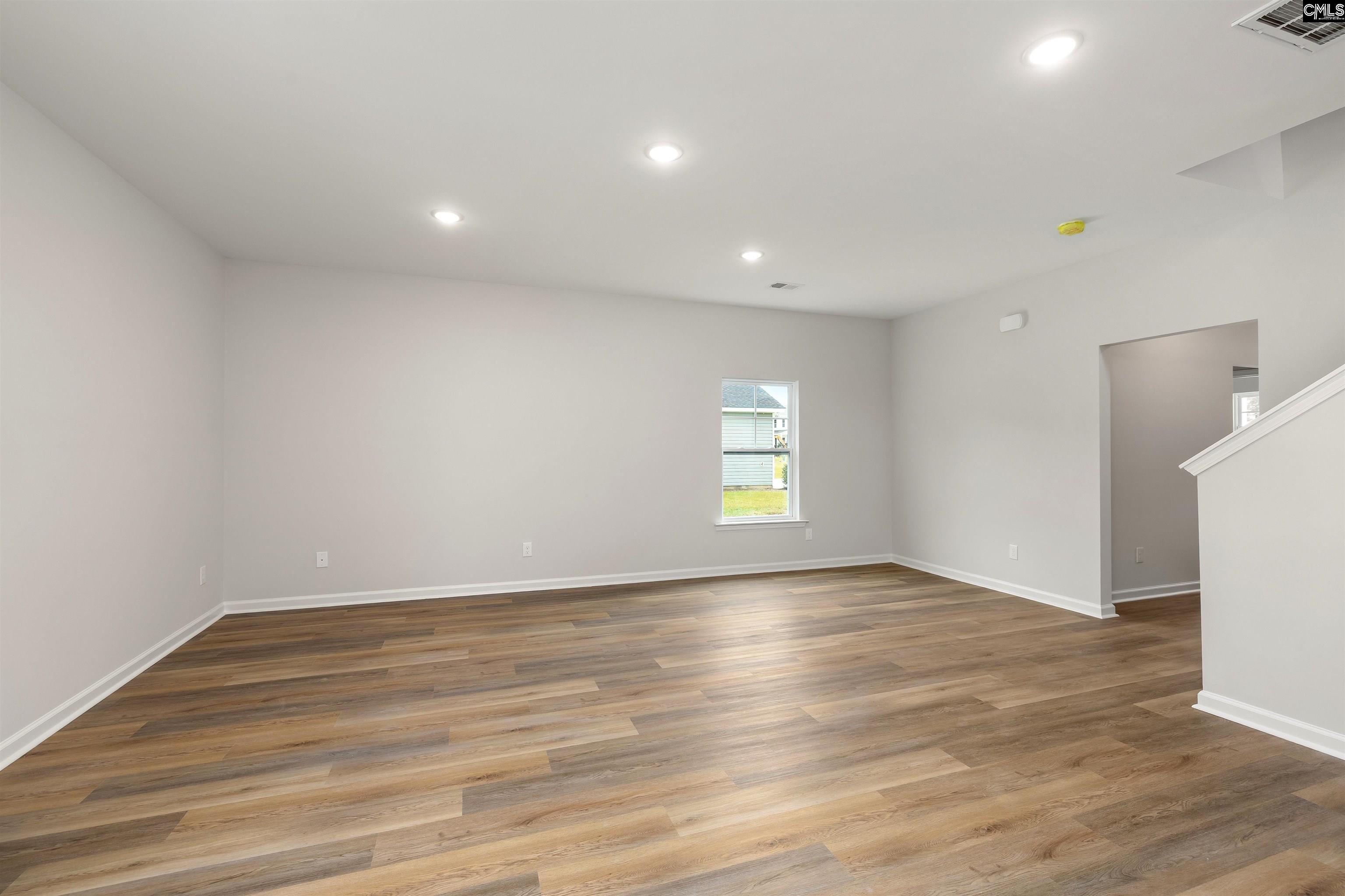Empty living room with brown plank flooring, recessed lights, and a window.