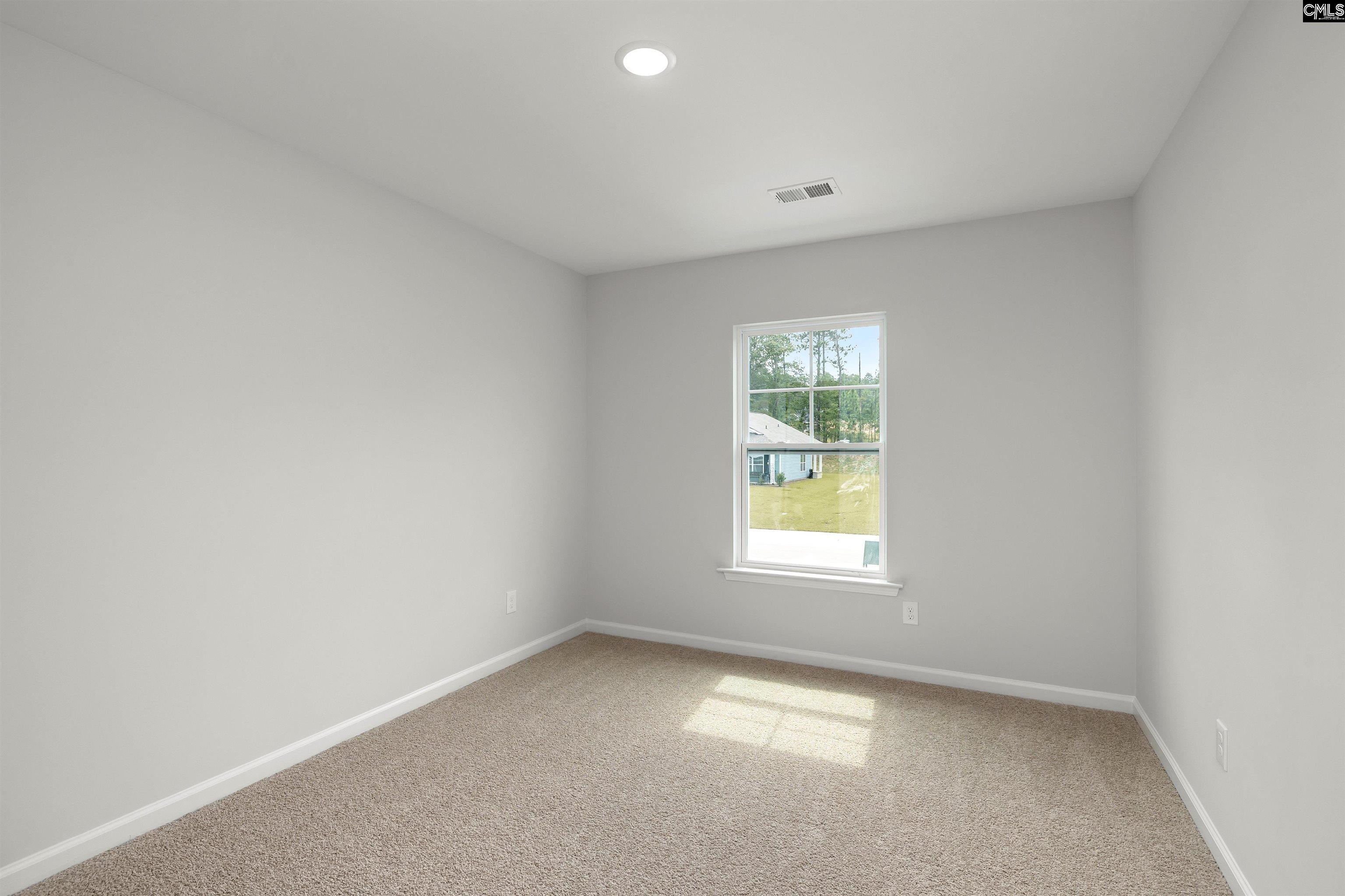Empty bedroom with beige carpet and a window overlooking a lawn and trees.