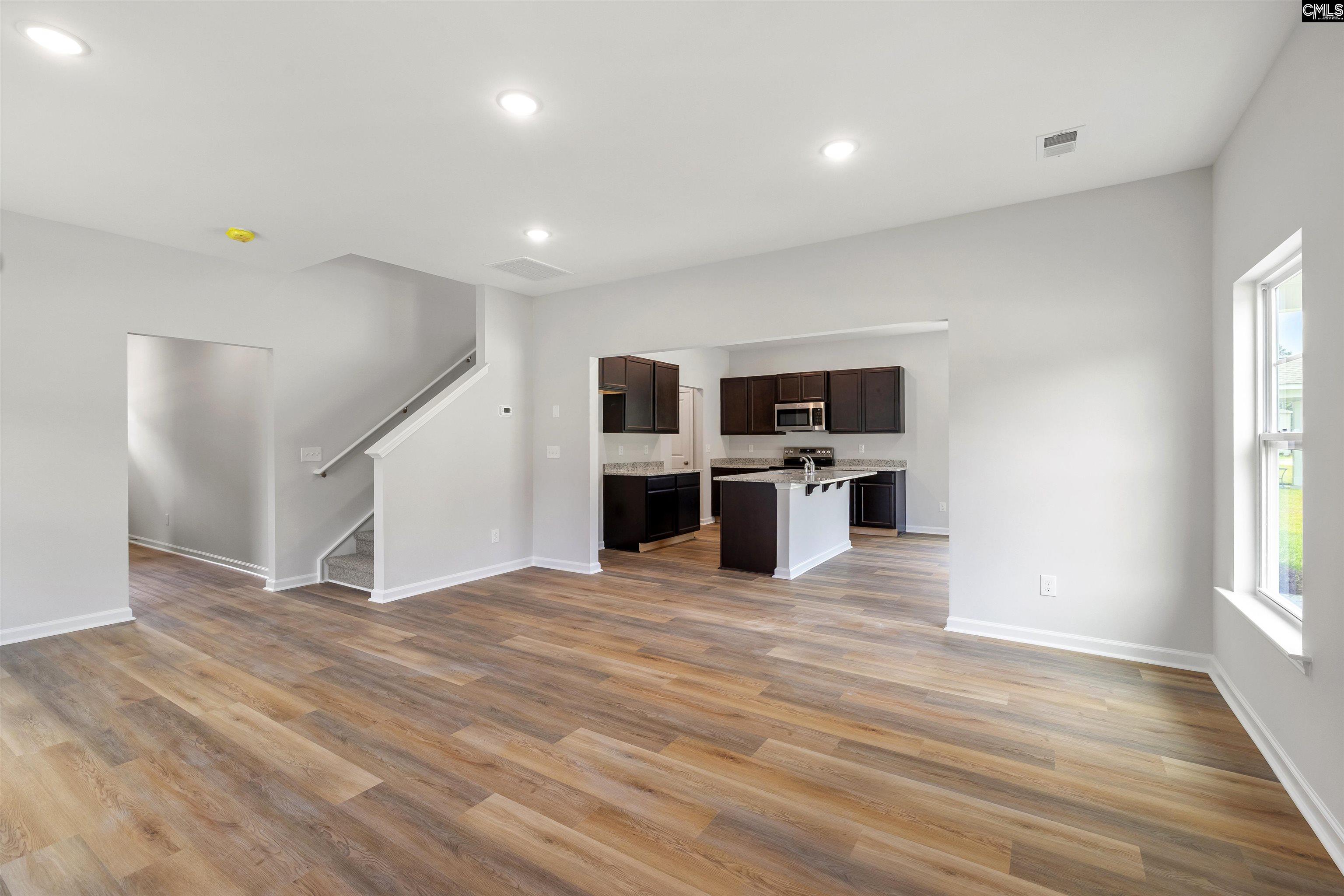 Unfurnished living area opening to a kitchen with a central island and dark cabinets.
