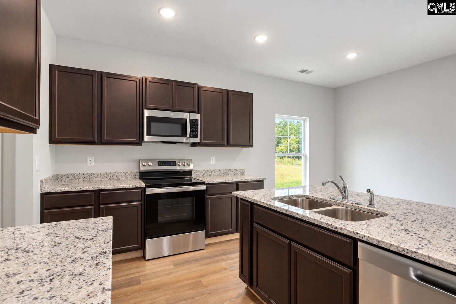 Kitchen with dark cabinets, granite counters, stainless appliances, and a large island with a double sink.