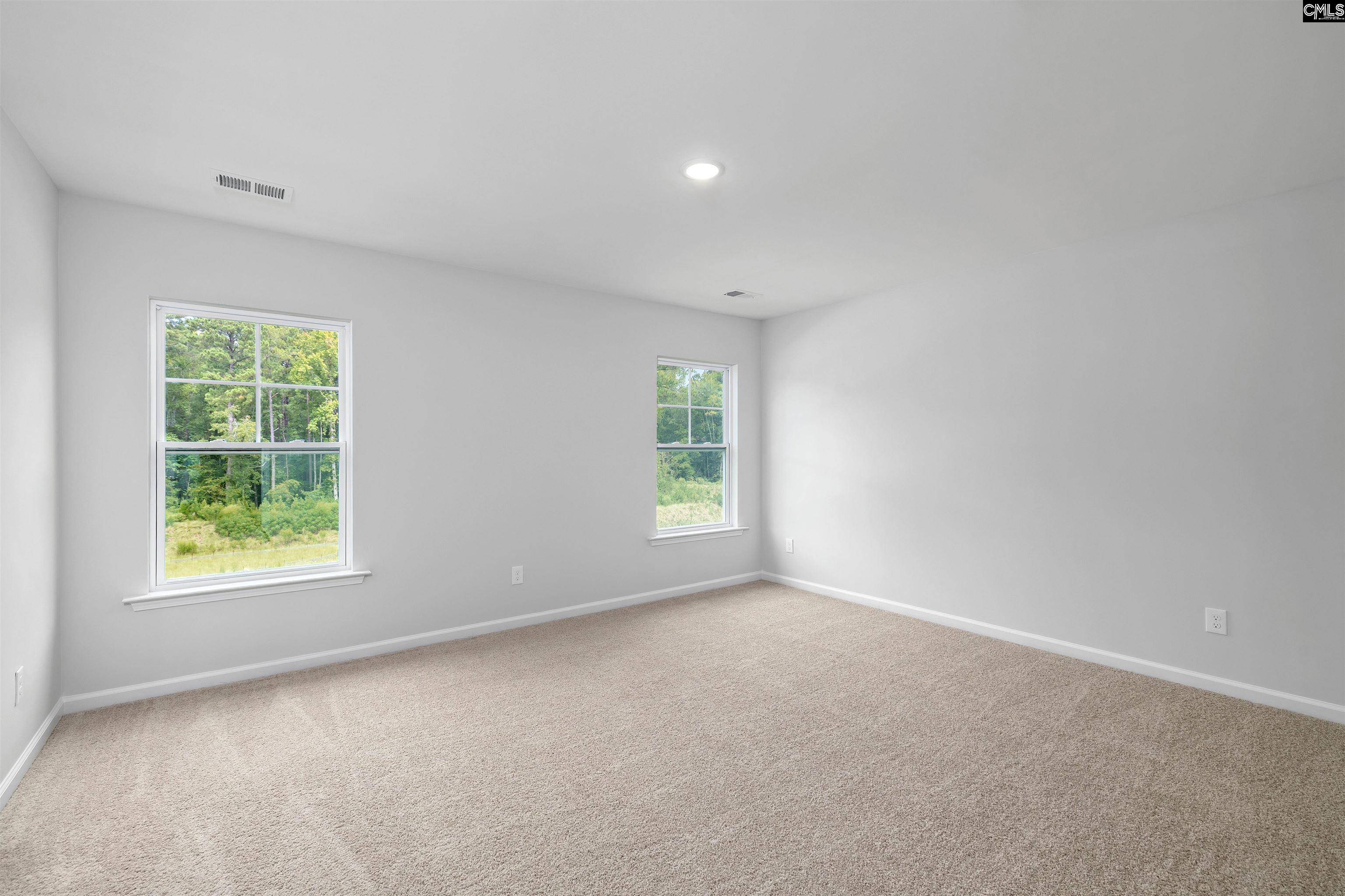 Empty carpeted room with two windows overlooking green trees.