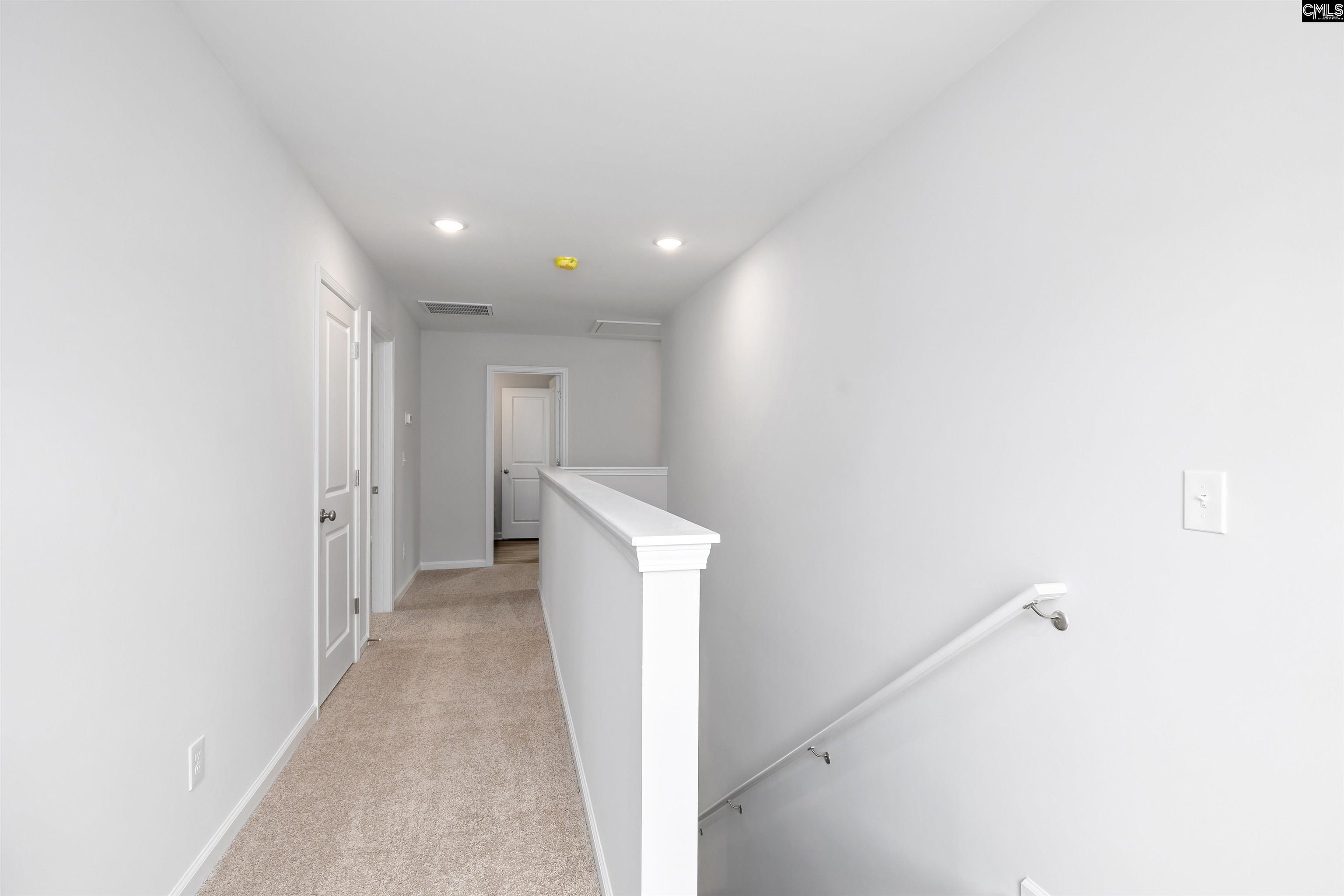 Empty carpeted upstairs hallway with white doors and a railing overlooking the stairs.