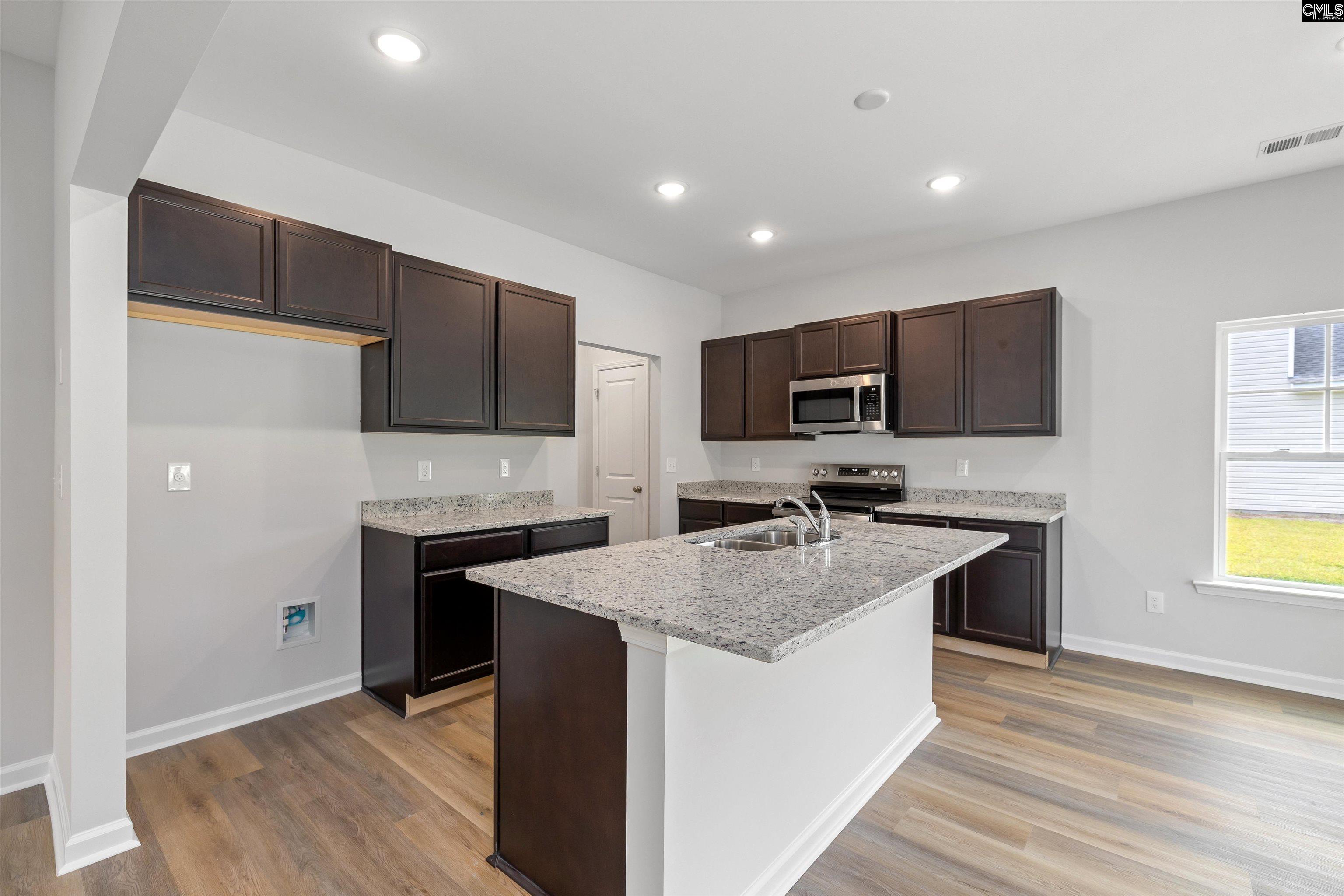 Unfurnished kitchen with dark cabinets, a granite island, stainless steel appliances, and wood-look flooring.