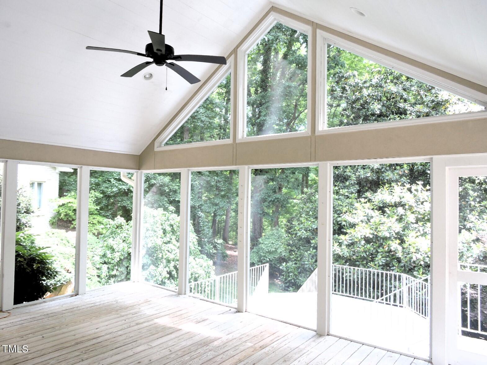 Sunroom with a vaulted ceiling, large windows, and views of leafy trees.