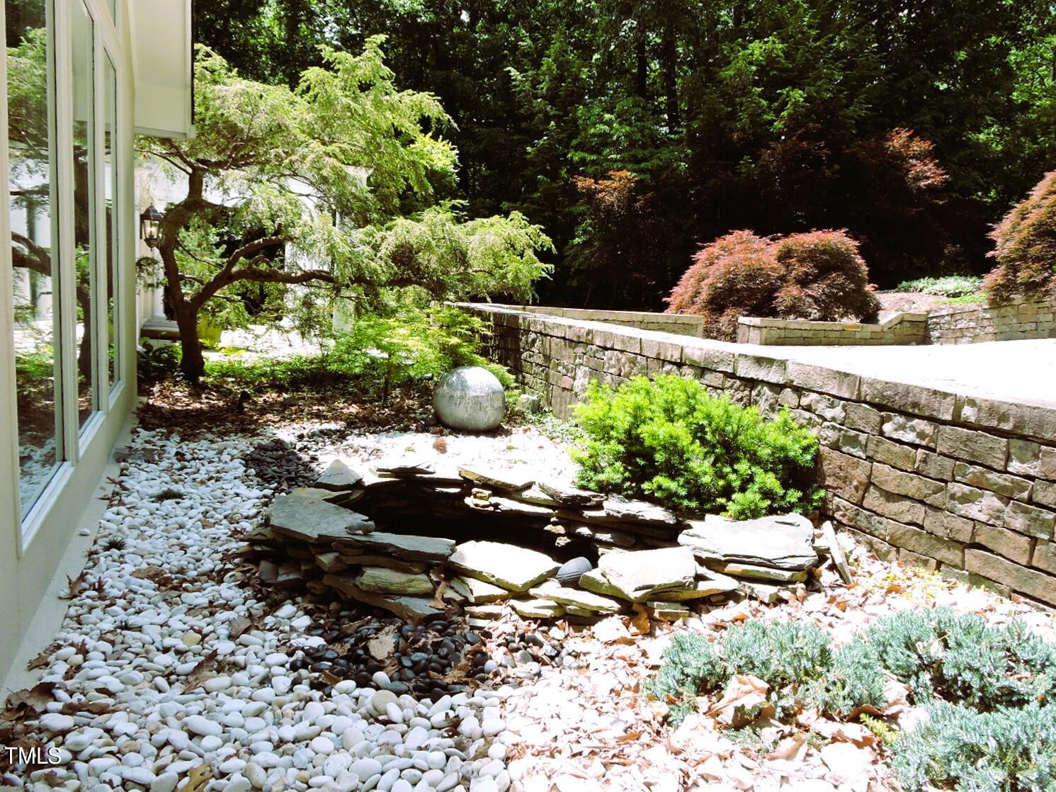 Landscaped garden beside a home with a stone wall and shallow rock water feature.
