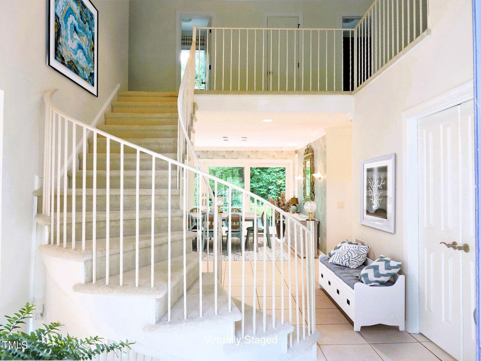 Curved carpeted staircase with white railings in a bright foyer, dining area visible beyond.
