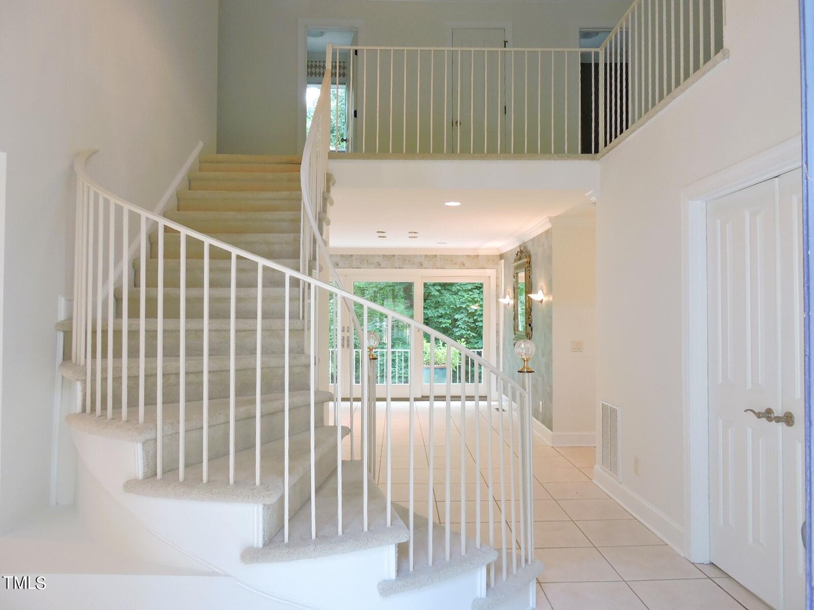 Curved carpeted staircase with white railings rises above a tiled foyer and glass doors.