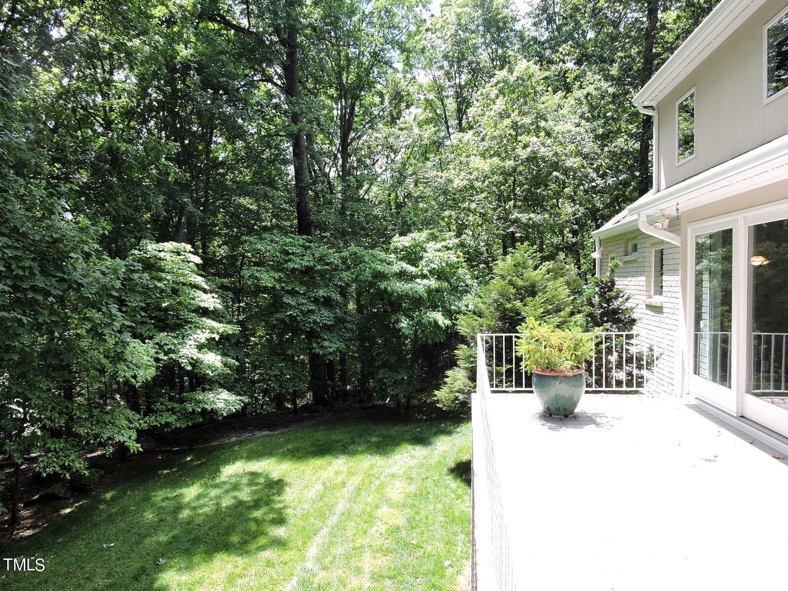 House beside a white-railed deck, with a potted plant, lawn, and wooded yard.