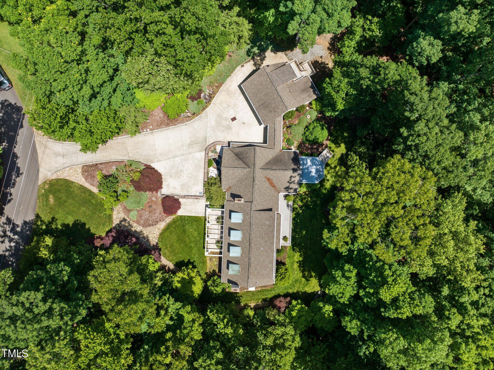 Aerial view of a house surrounded by trees, with a curved driveway and landscaped garden beds.