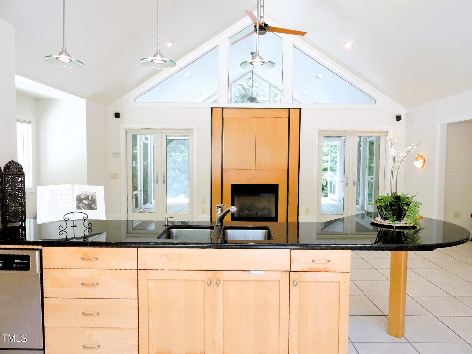 Kitchen with a large black-countertop island, vaulted ceiling, fireplace, and glass doors to the deck.