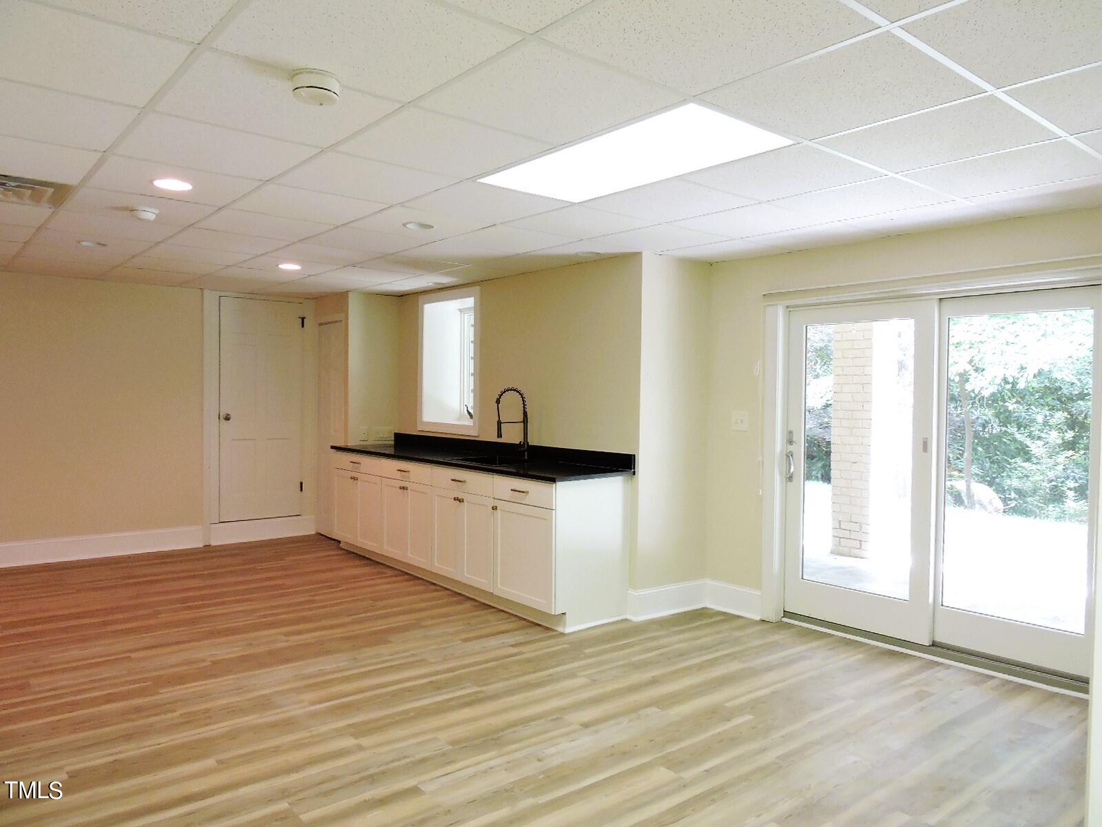 Vacant room with a white-cabinet kitchenette, black countertop, wood-look floors, and sliding glass doors.