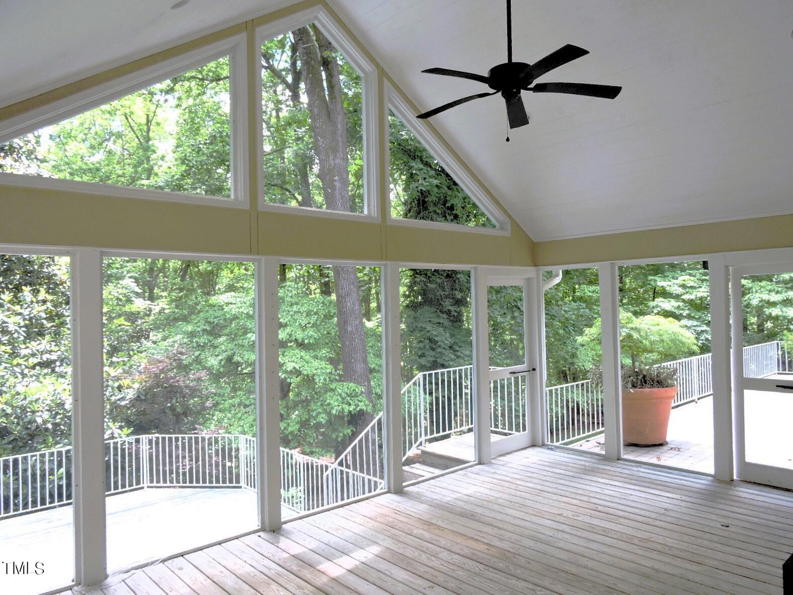 Enclosed sunroom with a vaulted ceiling, expansive windows, and views of leafy trees.