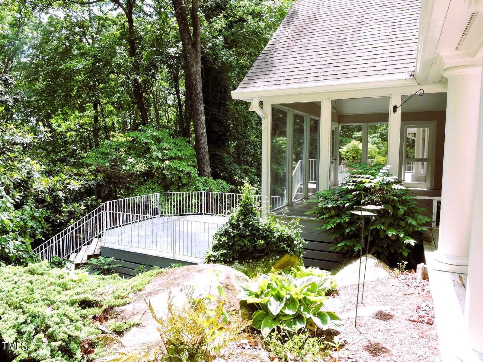 Raised deck and screened porch surrounded by leafy trees and landscaped garden beds.