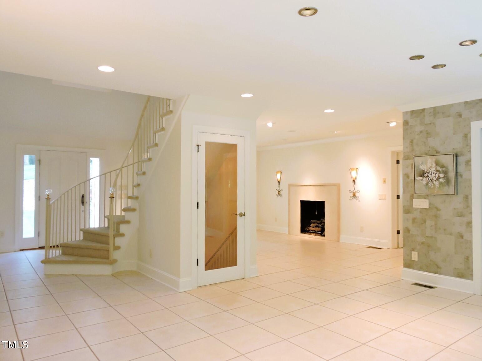 Vacant tiled living area with a curved staircase, entry door, fireplace, and stone accent wall.