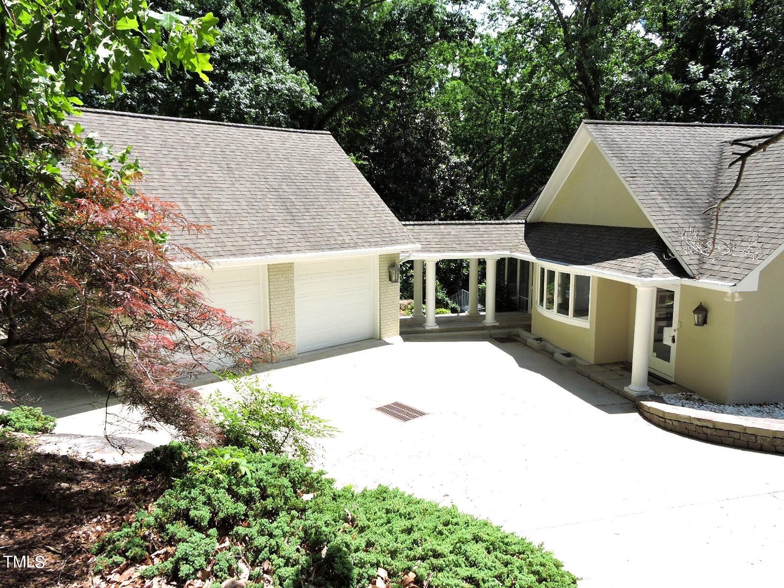 Home with a two-car garage, broad driveway, covered entry, and mature trees.