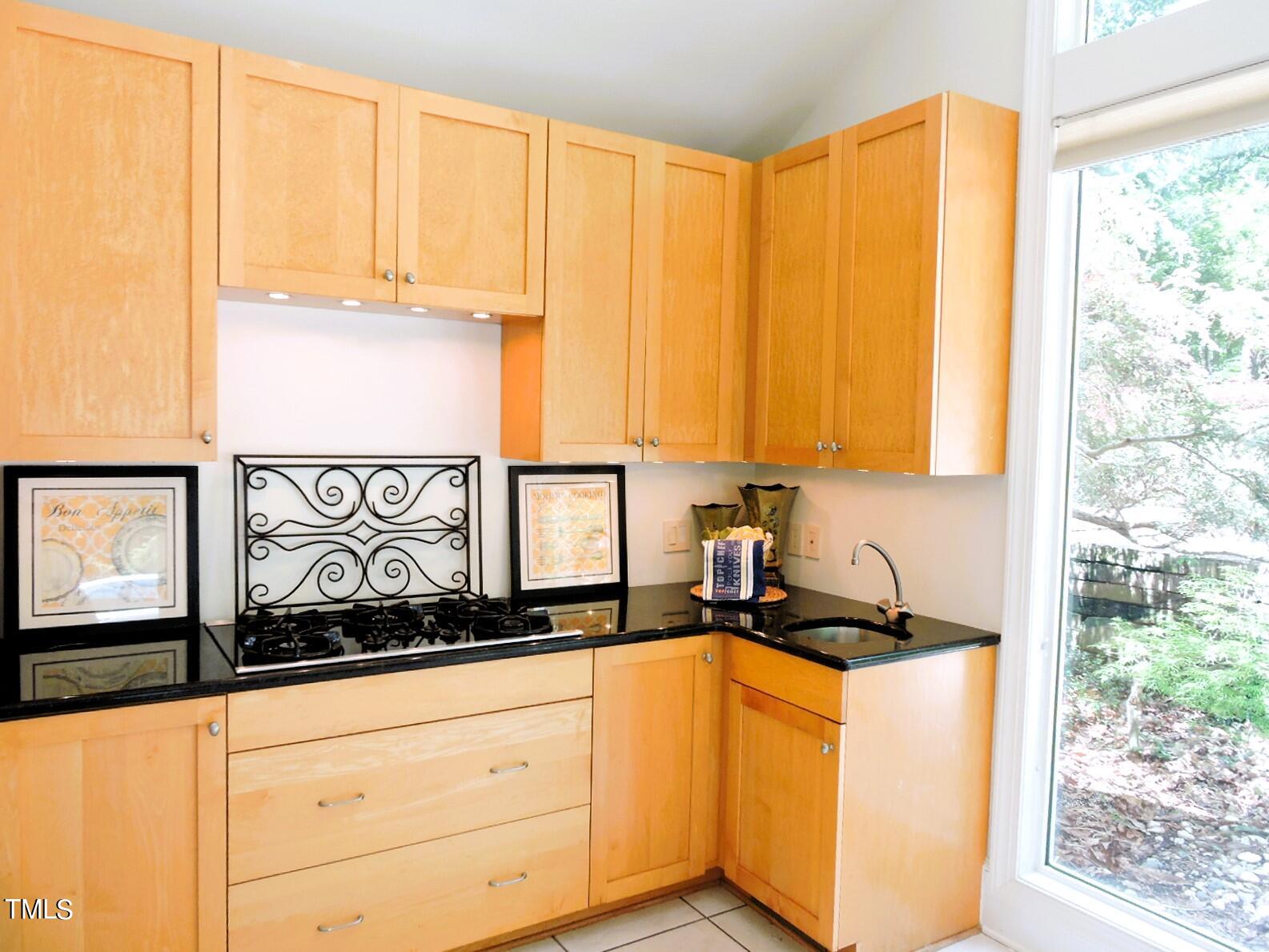 Kitchen with honey-colored cabinets, black counters, a gas cooktop, and a sink beside a glass door.