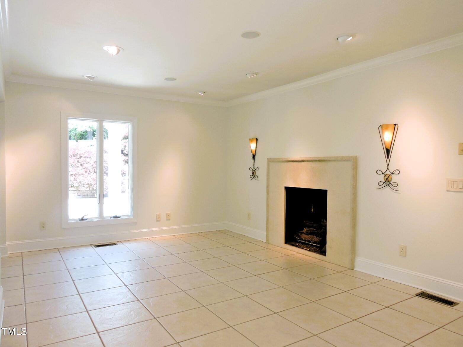 Empty tiled room with a fireplace, wall sconces, and a window overlooking the yard.