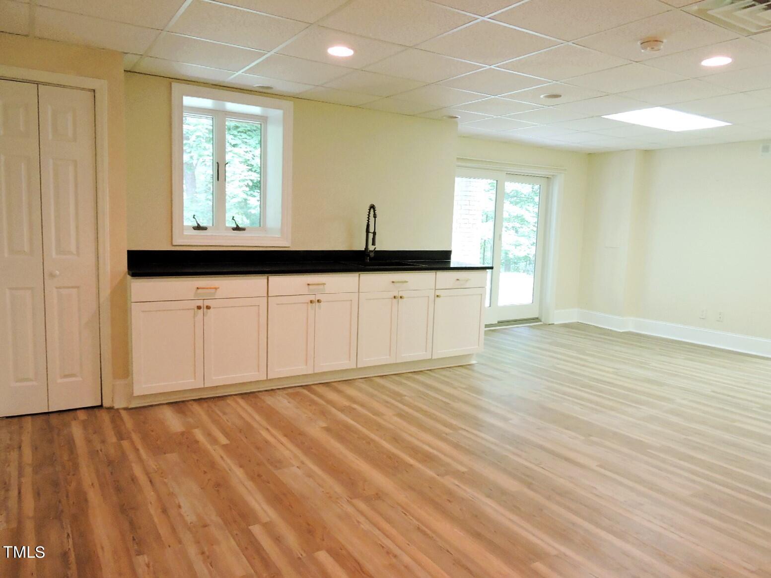 Kitchen with white cabinets, black countertops, wood-look floors, and glass patio doors.