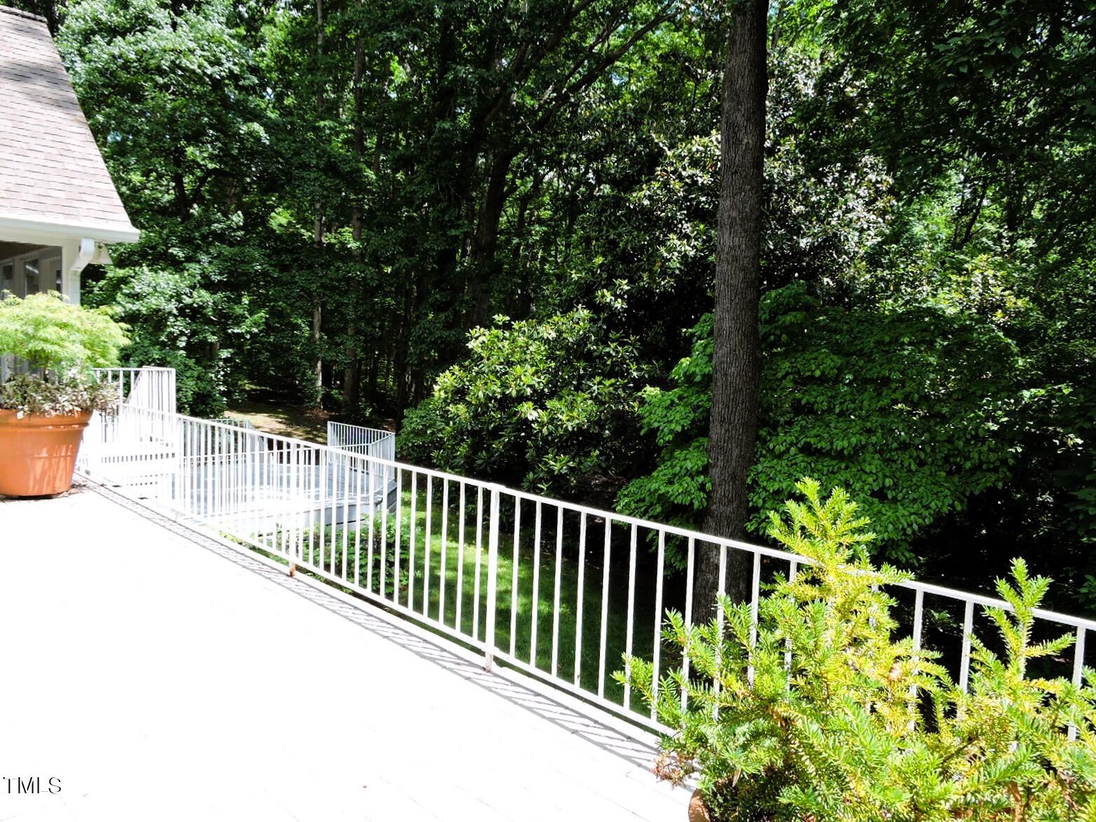 White deck overlooking a densely wooded yard, with railing and potted plants.