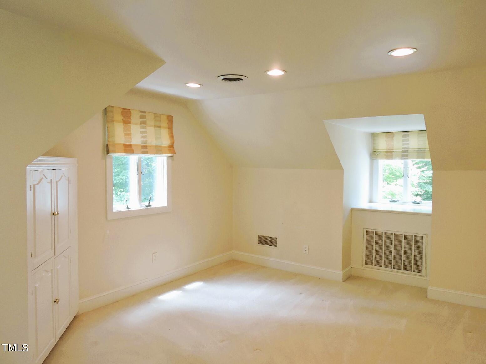 Empty bedroom with sloped ceilings, two shaded windows, and a built-in white cabinet.