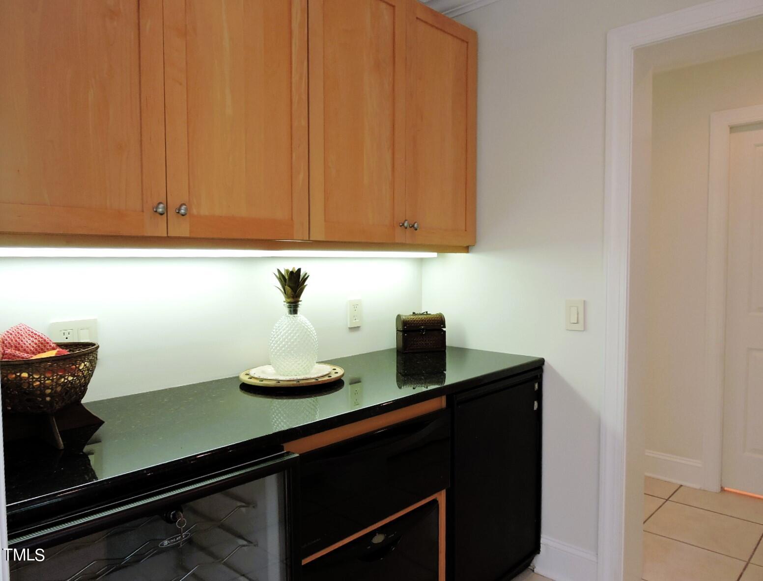 Wet bar with wood cabinets, a dark counter, and under-counter beverage appliances.