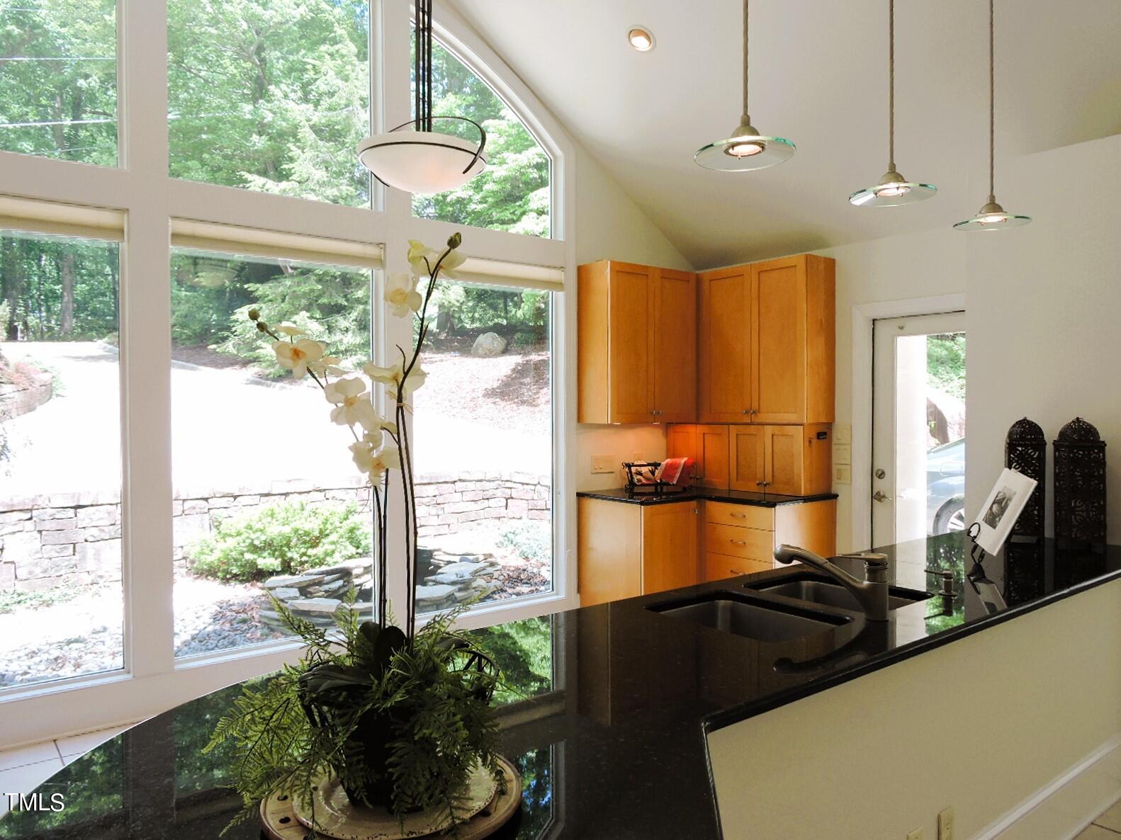 Kitchen with warm wood cabinets, a black island, and tall windows overlooking a leafy yard.
