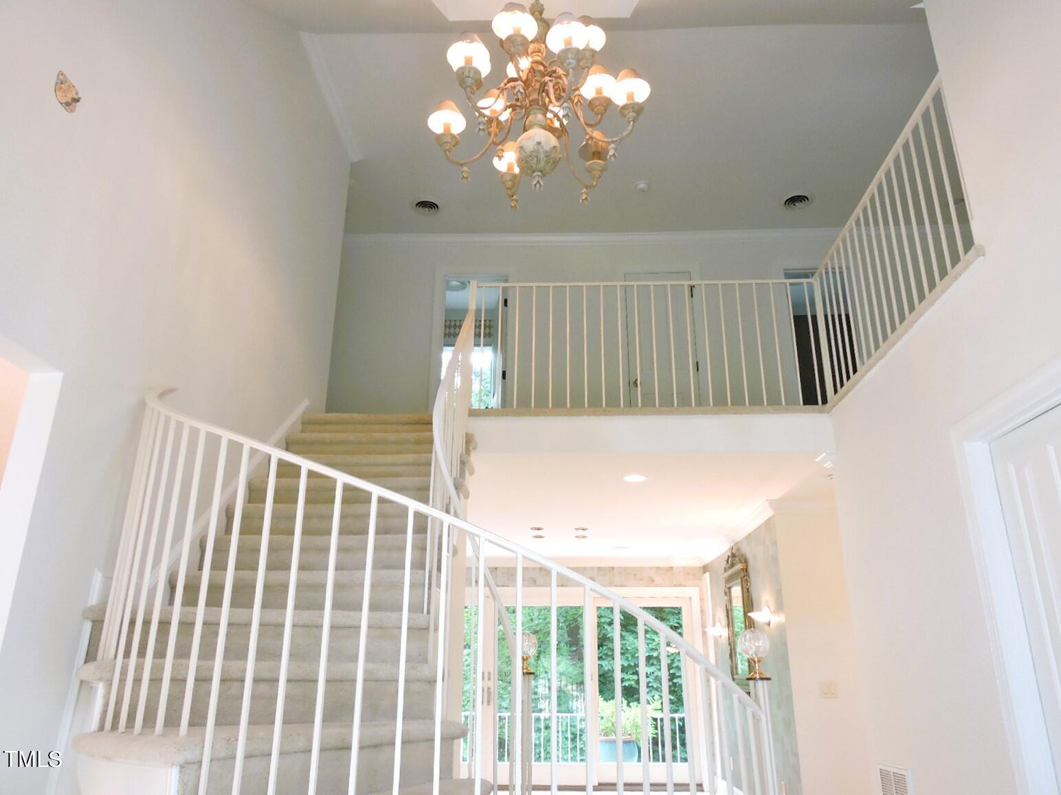 Two-story foyer with a curved carpeted staircase, white railings, and an ornate chandelier.