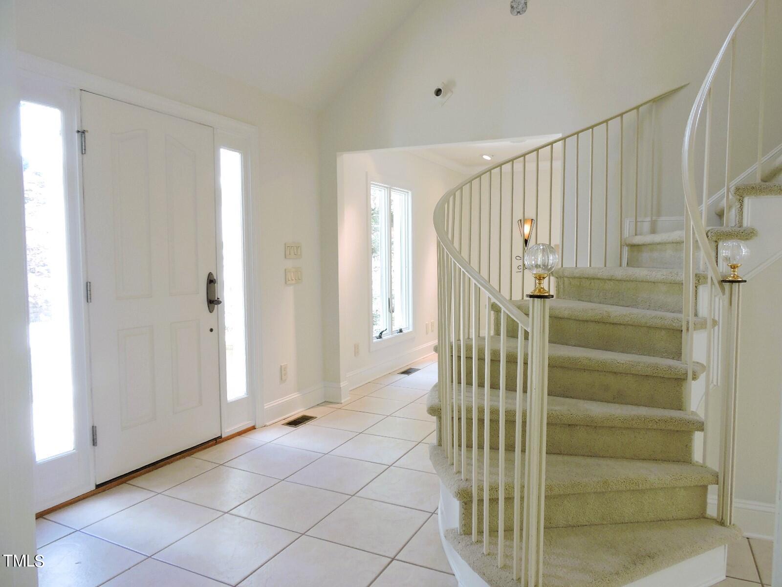 Entry foyer with tiled floors, a white front door, and a curved carpeted staircase.